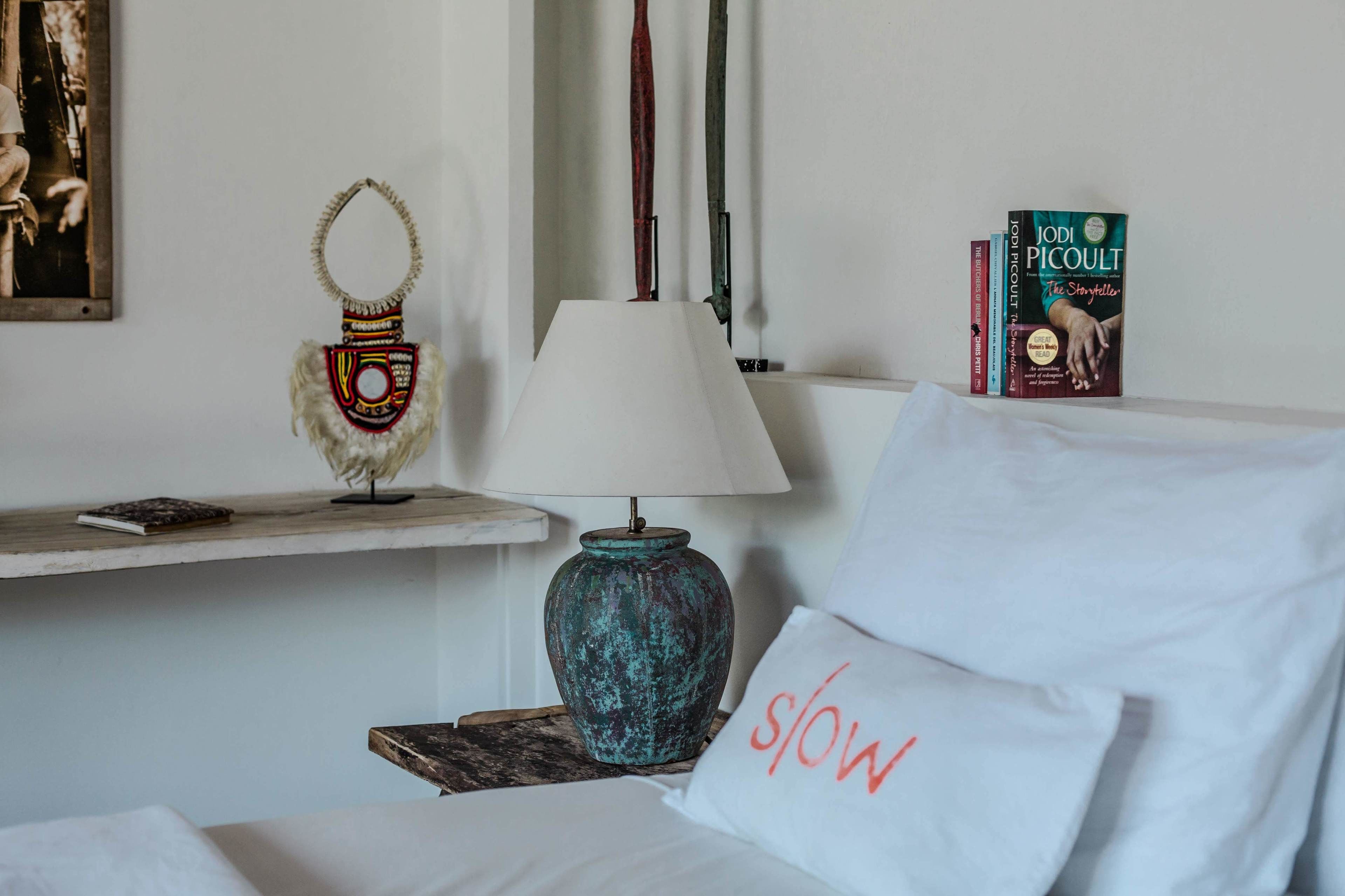 Una habitación de hotel ordenada con una cama, una lámpara, un objeto decorativo y un libro en una mesita de noche.