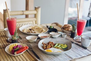 A table set with various dishes including a plate of eggs, avocado, and vegetables, and two glasses of red beverage.