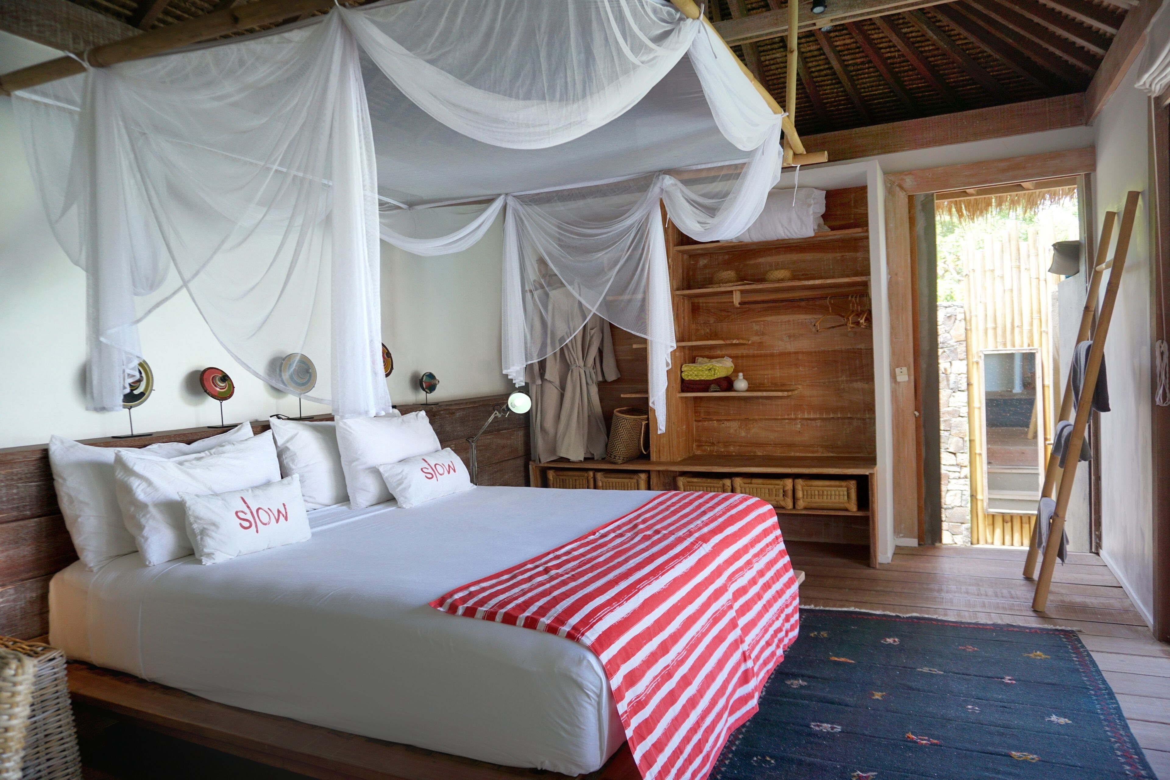 Une chambre à coucher avec un lit à baldaquin, une tête de lit en bois, des tables de chevet et une vue sur l’extérieur.