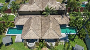A resort with thatched-roof structures, a swimming pool, and lush greenery. - Slow Private Pool Villas (Gili Air)