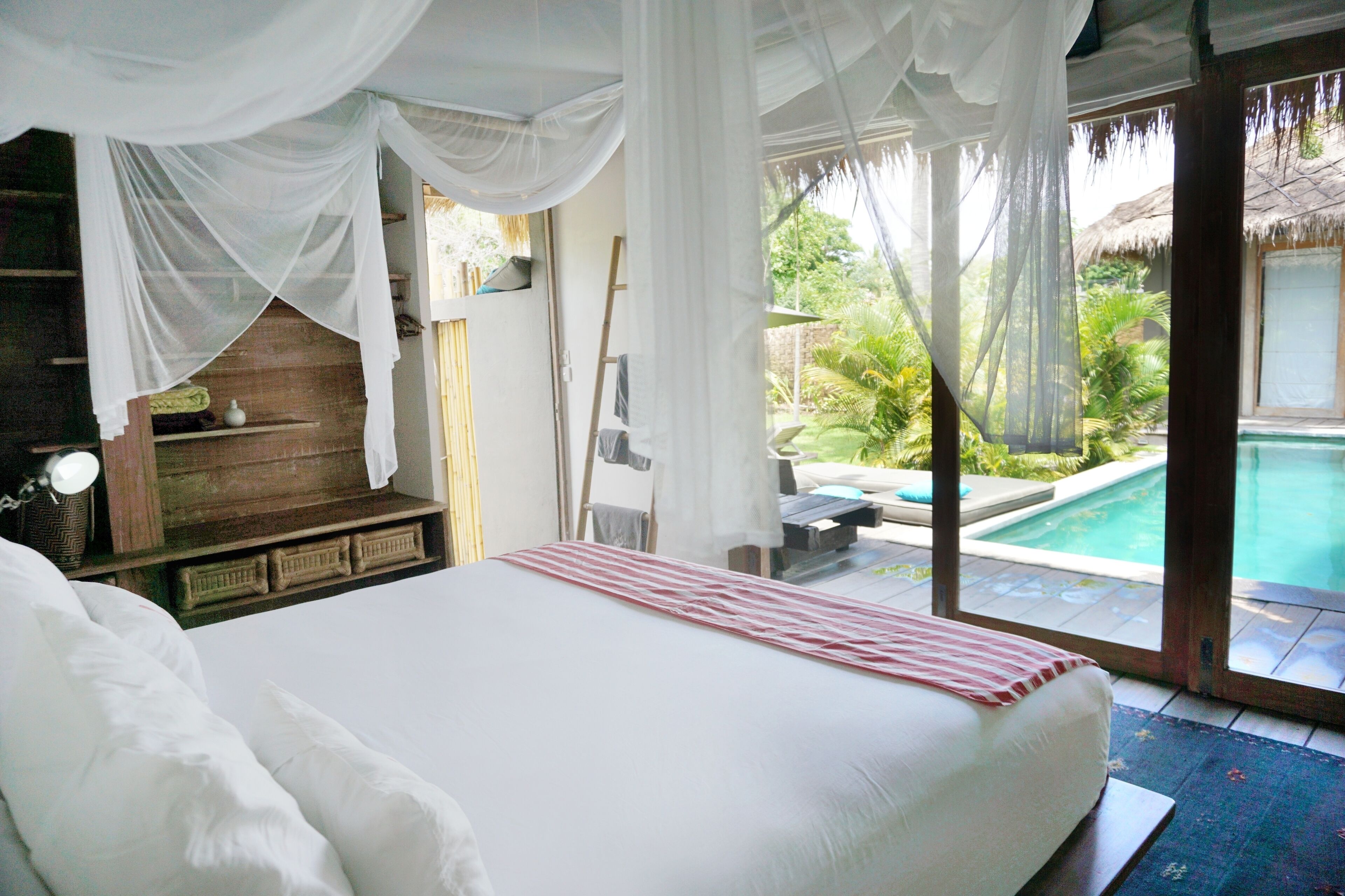 A bedroom with a large bed, white curtains, and a view of a swimming pool.