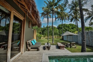 A wooden deck with a pool, outdoor furniture, and palm trees.