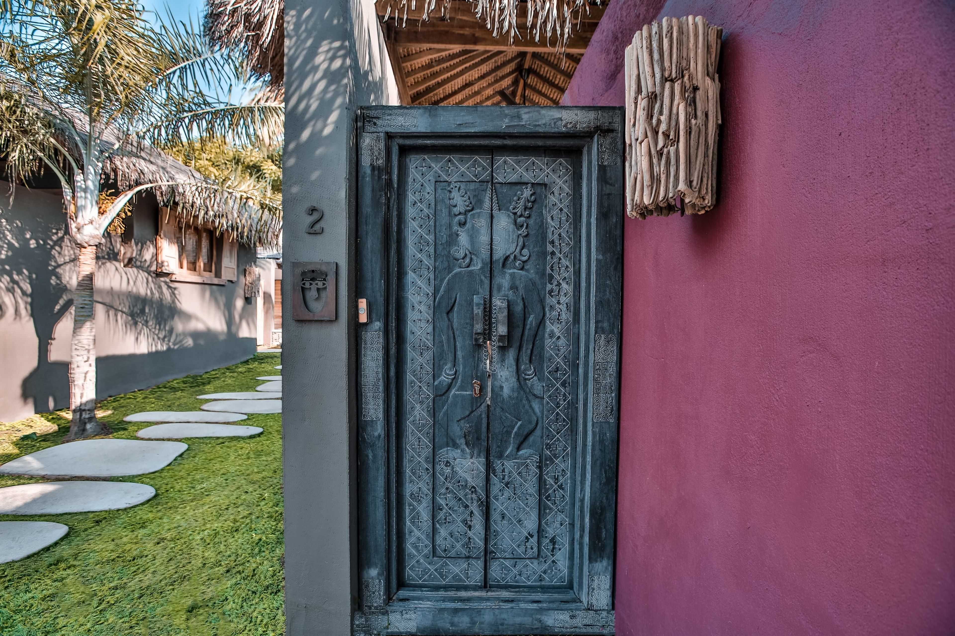 A door with intricate carvings, a number '2' sign, and a thatched roof structure in the background.