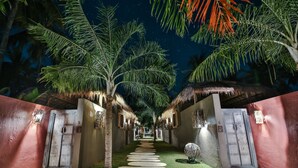 A pathway leading to a building with thatched roofs and palm trees, surrounded by walls and a night sky. - Slow Private Pool Villas (Gili Air)