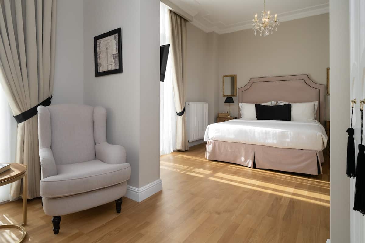 A hotel room with a large bed, a chair, a small table, and a radiator.