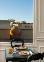 Mesa de jantar com itens de café da manhã e um vaso de plantas secas, com vista para um horizonte urbano e arquitetura histórica.
