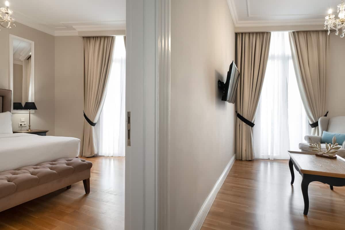 A hotel room with a bed, a TV mounted on the wall, a seating area with a table, and a chandelier.