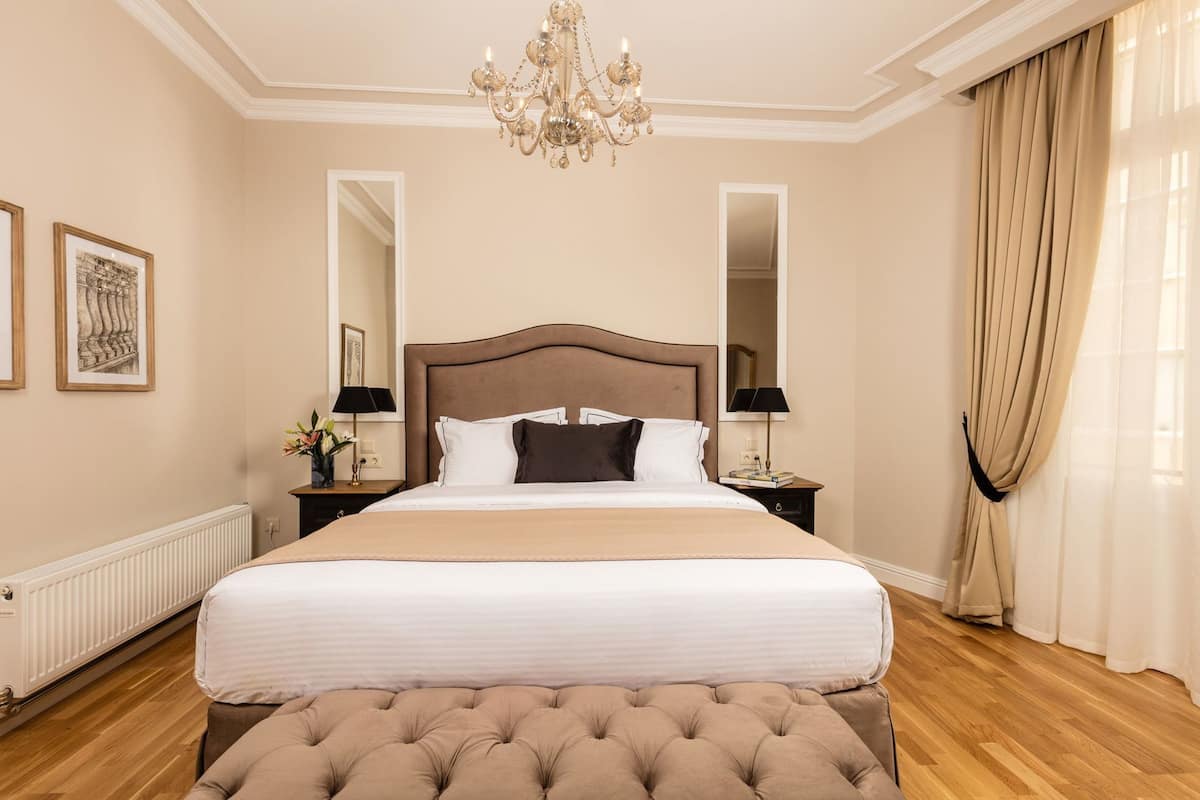 A hotel room with a large bed, a chandelier, a mirror, and a window with curtains.