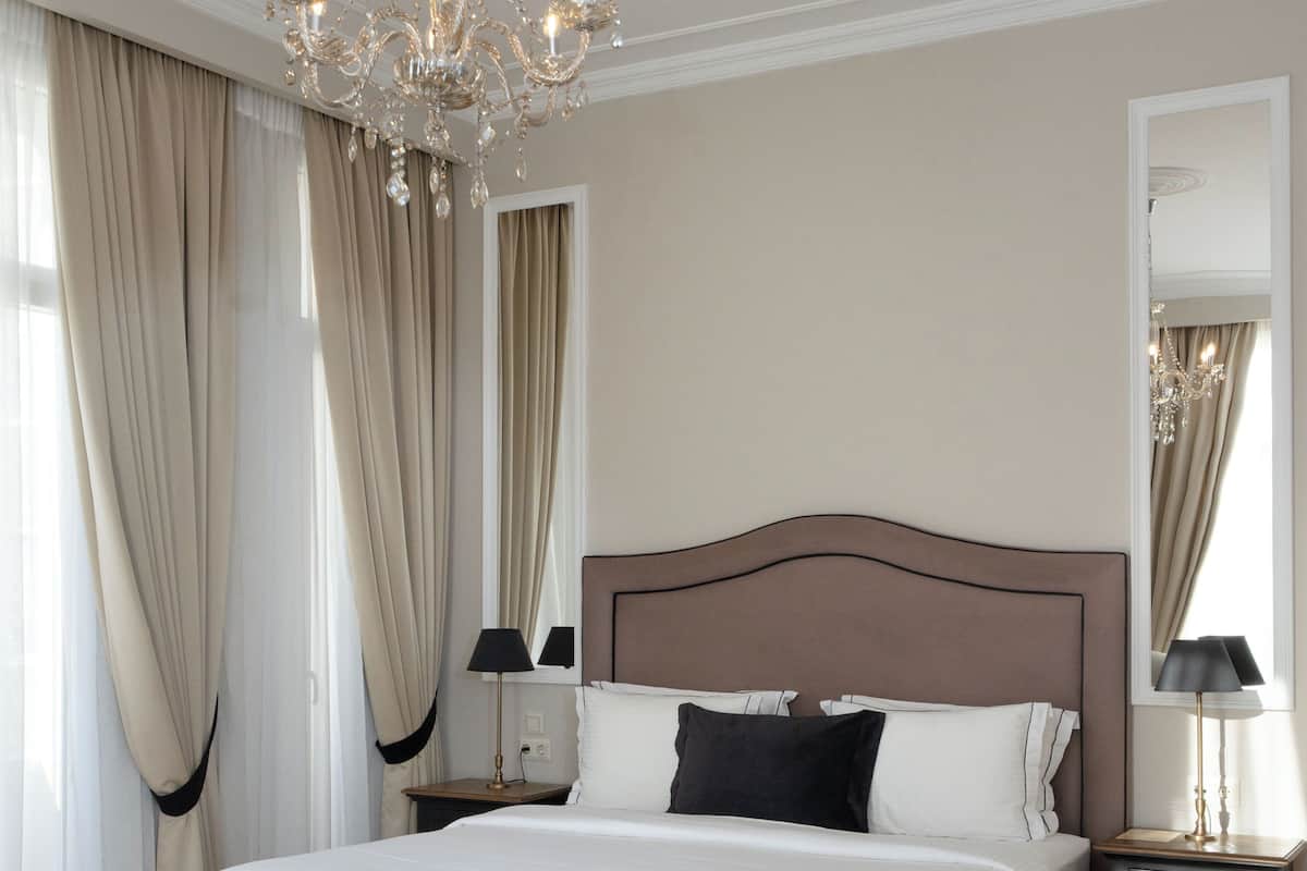 A spacious bedroom with a large bed, a tufted bench, a chandelier, and a nightstand with a lamp.