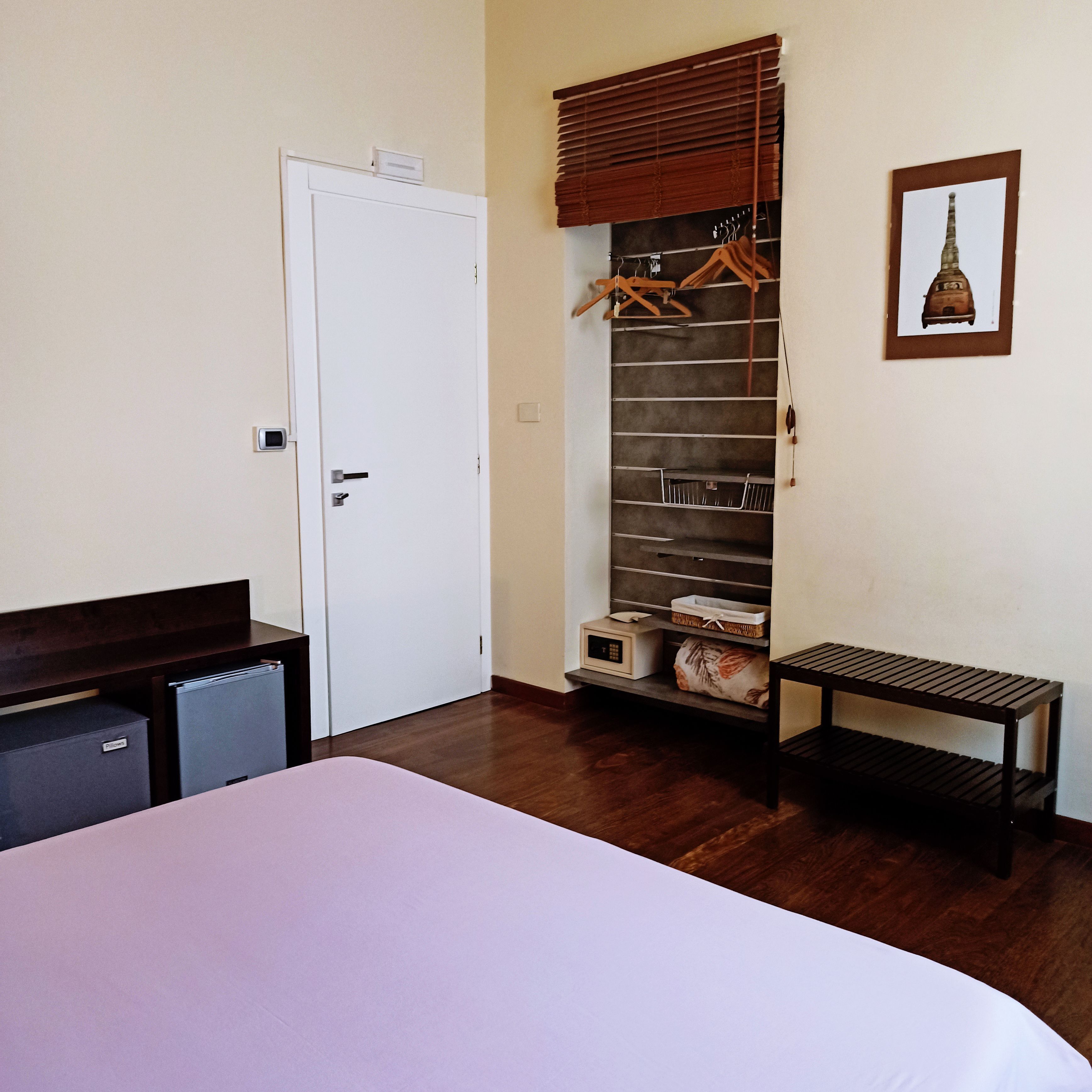 A bedroom with a bed, a wardrobe, a small table, and a hanging rack with clothes.