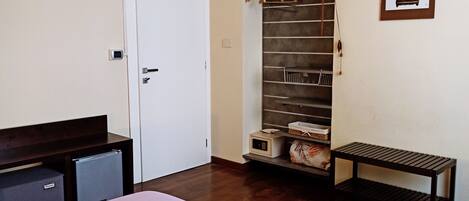 A bedroom with a bed, a wardrobe, a small table, and a hanging rack with clothes.