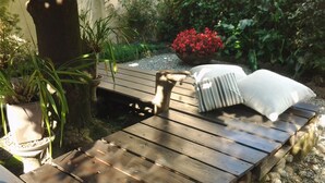 A wooden deck with a lounge chair and pillows, surrounded by potted plants and a red flower bush. - Colazione da Augusta (Turin)