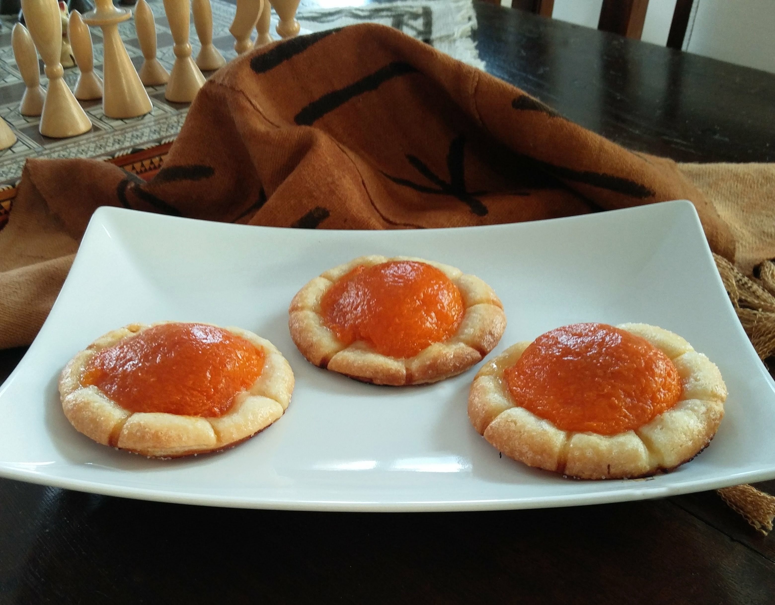 Un piatto bianco con tre piccole paste farcite all'arancia, su un tavolo di legno scuro.