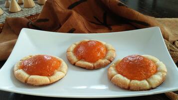 Un piatto bianco con tre piccole paste farcite all'arancia, su un tavolo di legno scuro.
