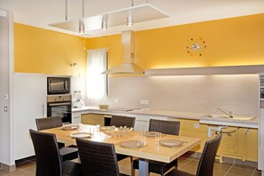 A modern kitchen with a dining area, equipped with a microwave, oven, and a sink. - Village de gîtes les hauts du Gevaudan (Montrodat)