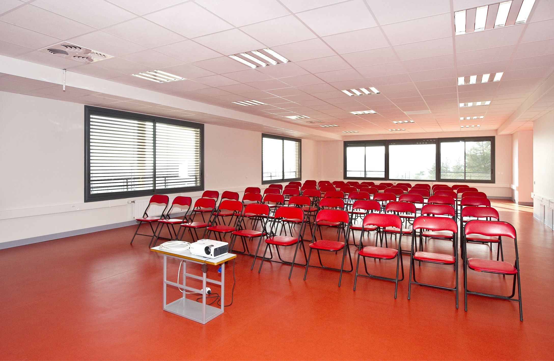 Ein Konferenzraum mit Reihen roter Stühle, großen Fenstern und einer weißen Decke mit Leuchtstofflampen.