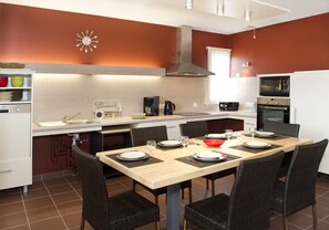 A modern kitchen with a dining table set for four, equipped with a microwave, oven, and coffee maker. - Village de gîtes les hauts du Gevaudan (Montrodat)