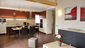 A modern kitchen with a dining area, featuring a wooden ceiling, a built-in oven, and a dining table with chairs. - Village de gîtes les hauts du Gevaudan (Montrodat)