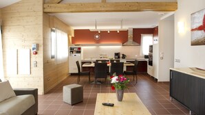 A modern kitchen with wooden beams, a dining area with chairs, and a living space with a sofa and a coffee table. - Village de gîtes les hauts du Gevaudan (Montrodat)