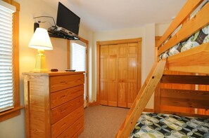 A bedroom with a bunk bed, a wooden dresser, a lamp, a television on a shelf, and a door. - Bottoms Up: Gorgeous oceanfront home, elevator, private heated pool, hot tub and (Nags Head)