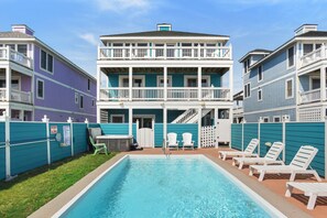 A two-story building with a swimming pool, white railings, and a covered patio area. - Bottoms Up: Gorgeous oceanfront home, elevator, private heated pool, hot tub and (Nags Head)
