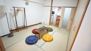 Una habitación japonesa tradicional con suelo de tatami, una mesa baja con cojines, un perchero y vistas a la cocina.