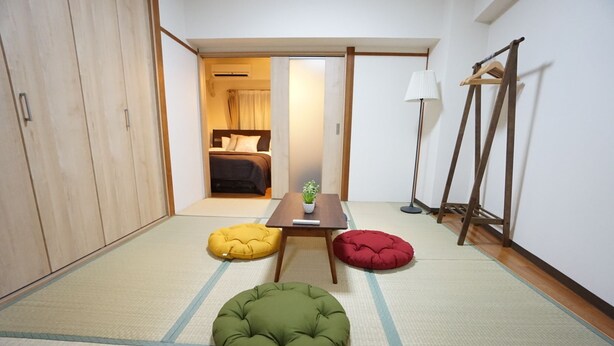 Una habitación con suelo de tatami, una cama, una mesa con una planta y una lámpara.