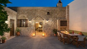 A stone courtyard with a dining area, potted plants, and a view into the interior. - Rodia House (Rhodes)