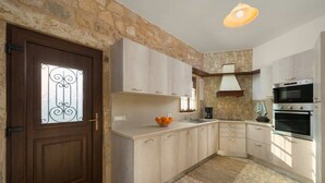 A kitchen with stone walls, wooden cabinets, a built-in oven, and a decorative door. - Rodia House (Rhodes)