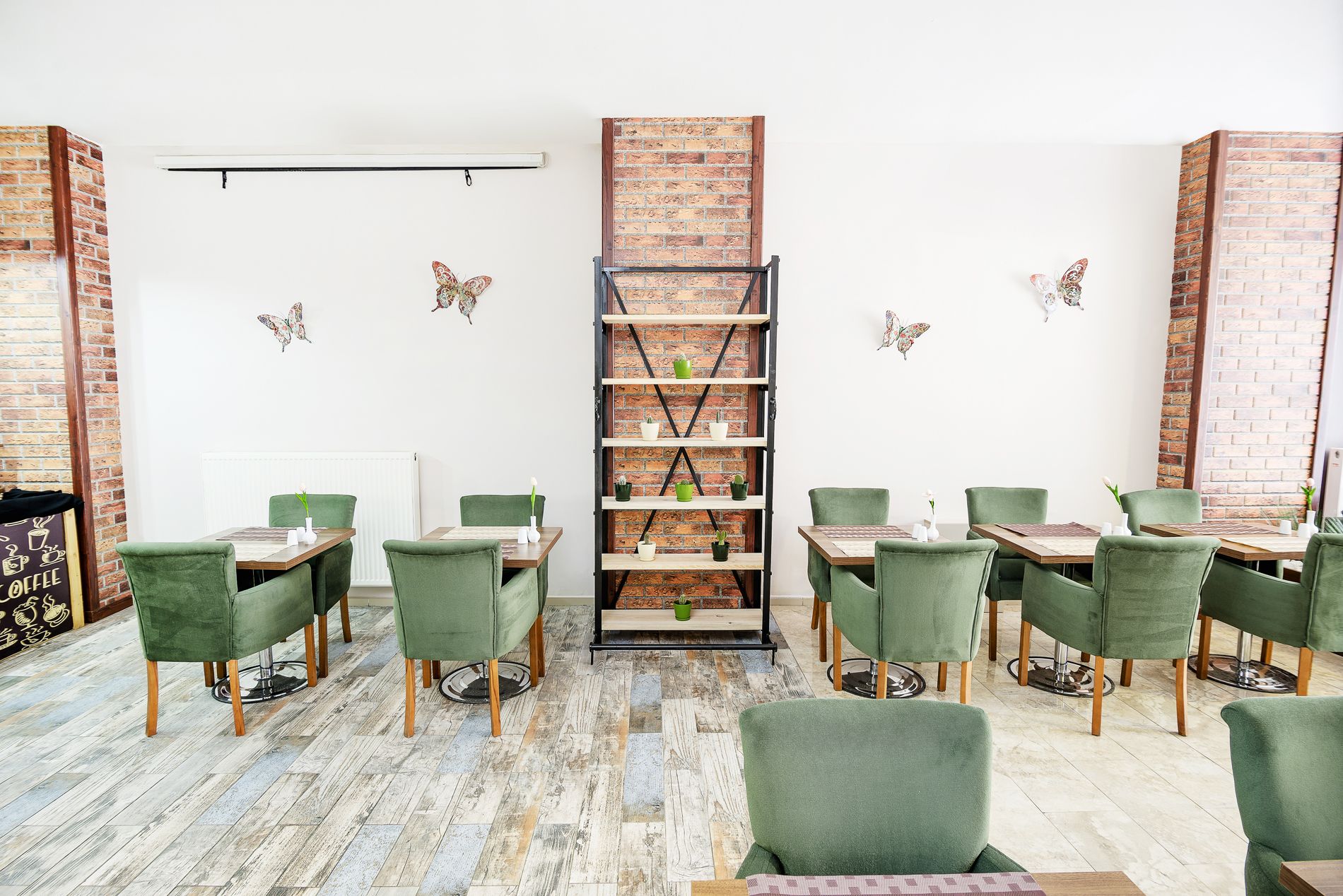 A dining area with green upholstered chairs, a brick wall, and a central shelving unit with potted plants.