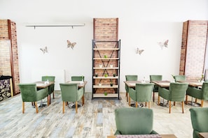 Un coin repas avec des chaises à revêtement vert, un mur en briques et une bibliothèque centrale agrémentée de plantes en pot.
