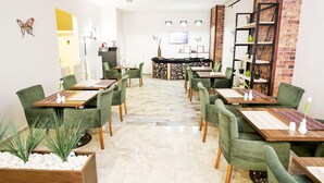 A modern dining area with green upholstered chairs and wooden tables, a brick accent wall, and a reception desk in the background. - The Corner Inn Hotel Suit (Eskisehir)