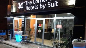 A hotel exterior with a neon sign, outdoor seating, and a large planter. - The Corner Inn Hotel Suit (Eskisehir)