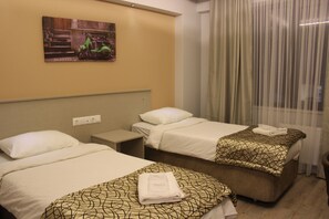 A hotel room with two single beds, a nightstand, a power outlet, and a window with curtains.