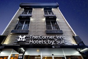 A hotel named "The Corner Inn Hotels by Suit" with a brick facade and illuminated signage.
