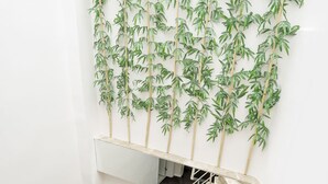 A staircase with beige marble steps and a metal handrail, leading to a white wall with a bamboo plant wall hanging. - The Corner Inn Hotel Suit (Eskisehir)