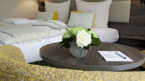 Une chambre d’hôtel bien rangée, avec un lit, une table ronde ornée d’un vase de fleurs et une lampe fixée au mur.