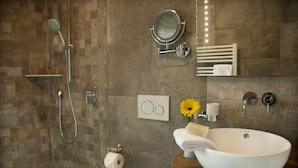 Une salle de bain moderne dotée d’un grand lavabo sur colonne, d’une douchette à main, d’un porte-rouleau de papier toilette et d’un miroir avec éclairage intégré.