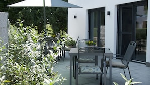 Un espace extérieur aménagé en terrasse, avec des tables et des chaises, un parasol vert et des plantes en pot.