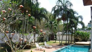 Une piscine dont le bord est revêtu de carrelage, entourée de palmiers et agrémentée d’un petit jardin avec des chaises longues blanches.