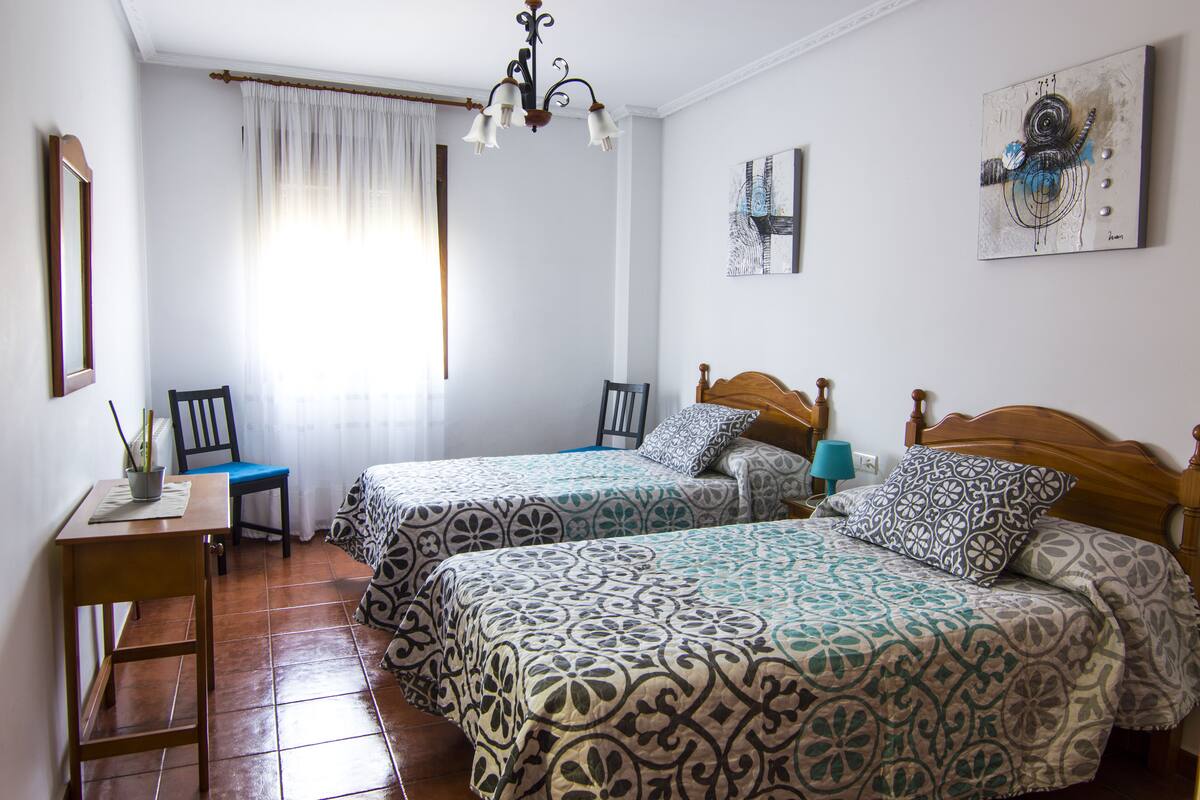 Une chambre avec deux lits, un bureau, des chaises et une fenêtre avec des rideaux.