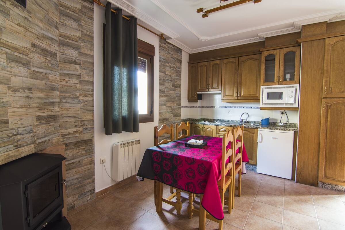 Une cuisine avec des meubles de rangement en bois, un four à micro-ondes, un petit réfrigérateur et une table à manger recouverte d’une nappe.