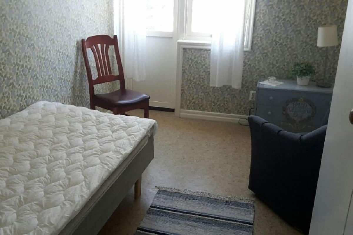 Une petite pièce, peu meublée, avec un lit, une chaise, une petite table et un radiateur.