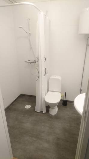 A small, white bathroom with a shower, toilet, and sink.