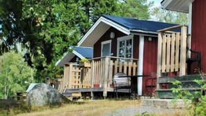 Une cabane rustique dotée d’un porche en bois et d’une façade rouge.