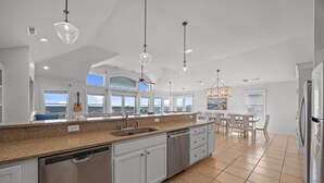 A spacious kitchen with a granite countertop, stainless steel appliances, and a dining area with a view. - Atlantic Watch: Oceanfront | 14 bedrooms | Private Walkway | Heated Private Pool (Kill Devil Hills)