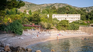 A beach with a rocky shoreline, a pool, and a building with multiple balconies.