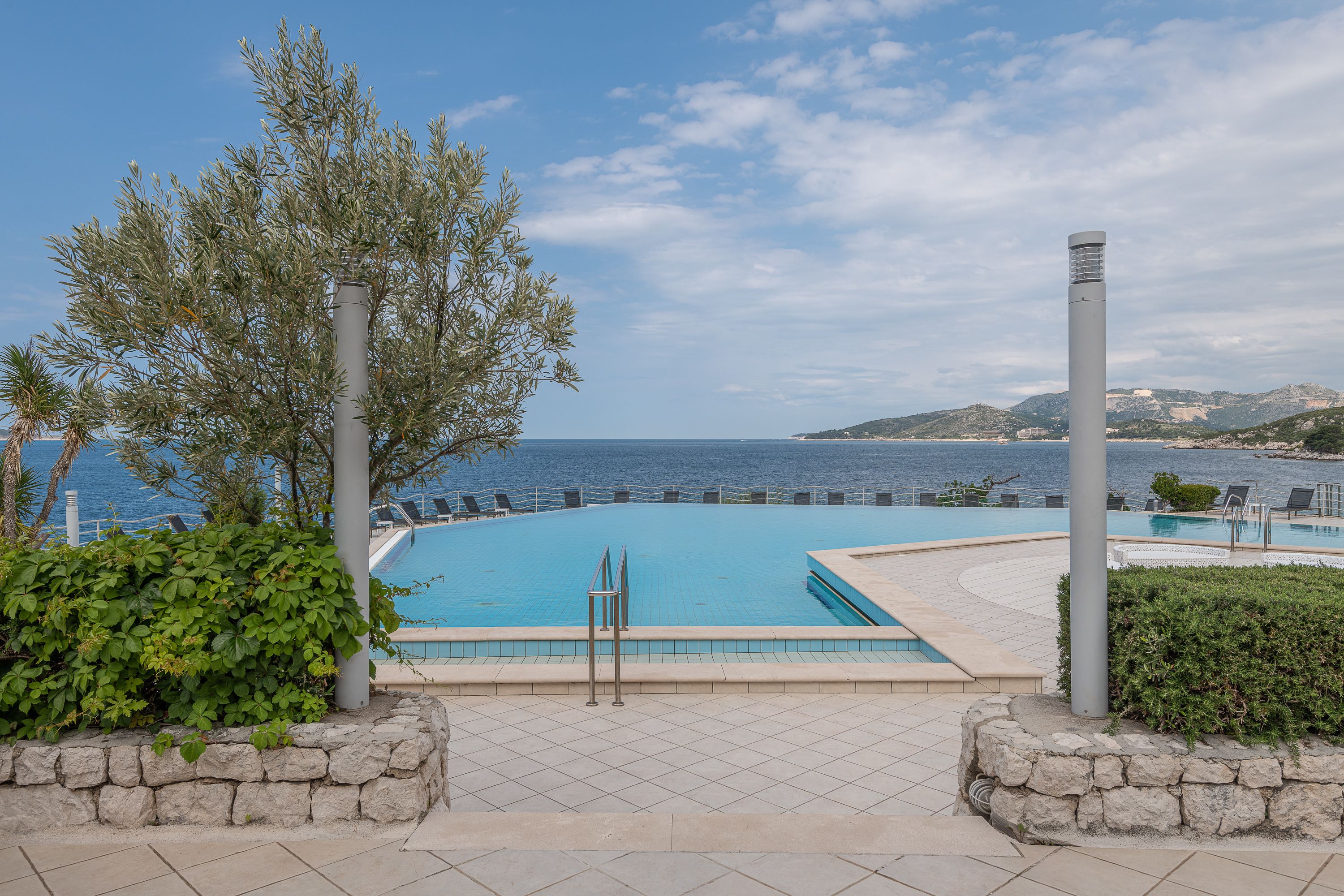 A swimming pool with a view of the sea and hills in the background.