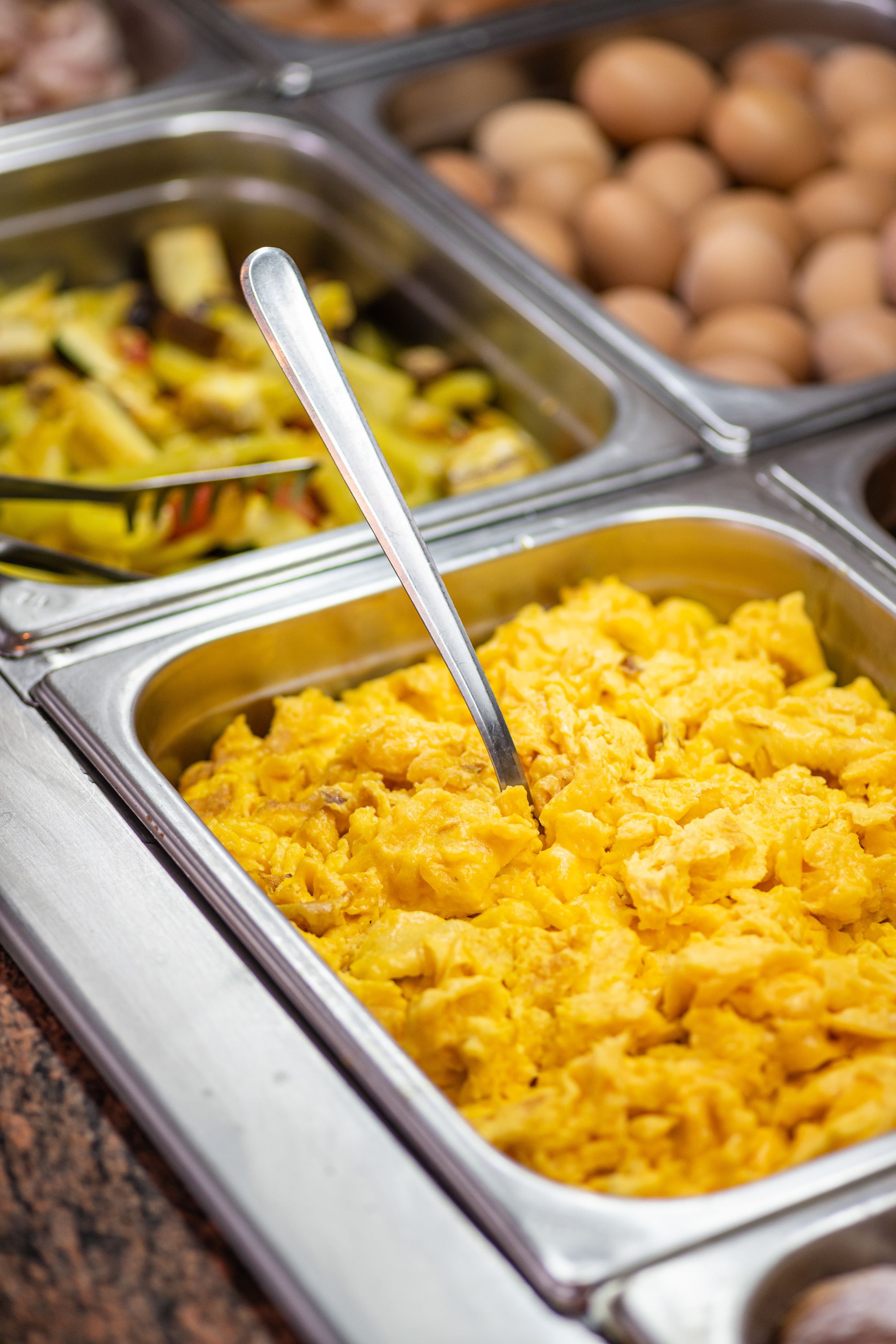 A buffet with various food items including scrambled eggs, vegetables, and potatoes.