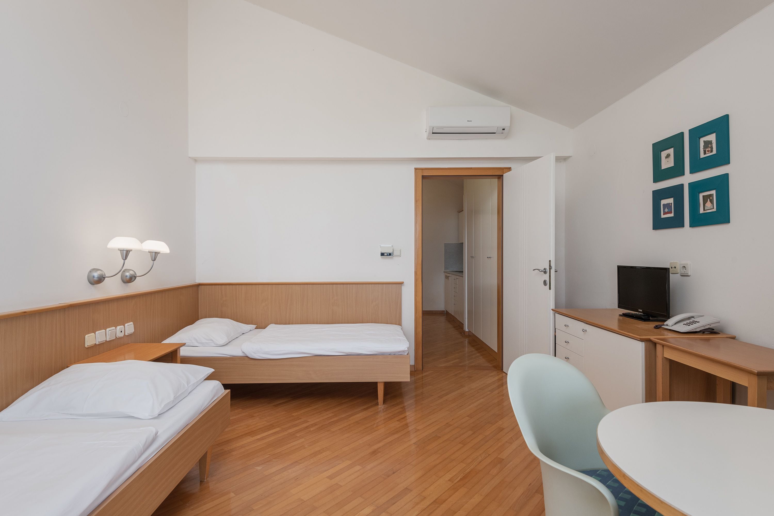 Ein Hotelzimmer mit zwei Einzelbetten, einem Schreibtisch mit Stuhl, einem Fernseher und einer Klimaanlage.